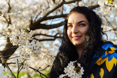 Attractive young brunette woman with long hair smiling in spring in blooming cherry blossom garden
