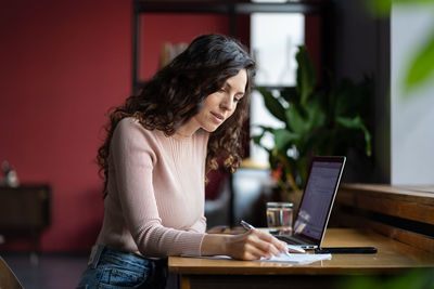 Focused young woman auditor doing paperwork at workplace in office, preparing financial statement