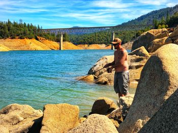 Full length of shirtless man standing on rock against sky