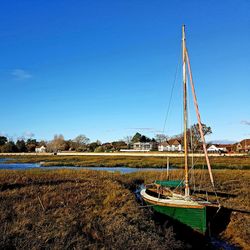 Sailboats moored on shore against clear blue sky