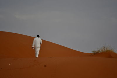 Rear view of man walking on sand dune