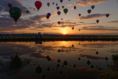 Hot air balloons flying over lake against sky during sunset