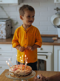 Cute toddler boy in yellow t-shirt smiling near the birthday cake
