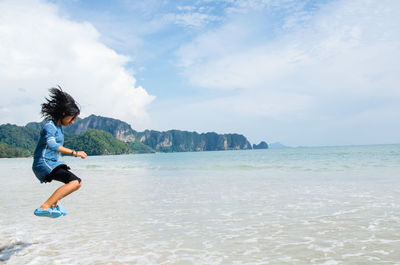 Full length of teenage girl jumping against sea at beach