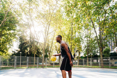 Focused african american sportsman in activewear standing on sports stadium and holding basketball ball