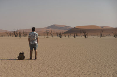 Rear view of man walking on desert against clear sky