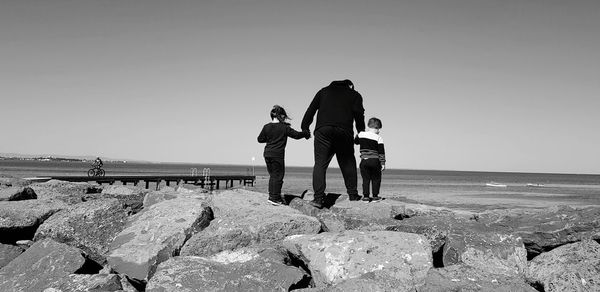 People on rocks at beach against clear sky