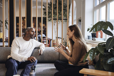 Businesswoman discussing with male colleague while sitting on sofa at coworking office