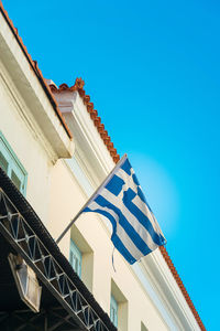 Low angle view of flag waving on building against clear blue sky