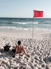 Rear view of shirtless man sitting on beach