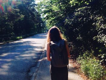 Rear view of woman with backpack standing on road amidst trees in forest