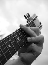 Close-up of hands playing guitar against sky