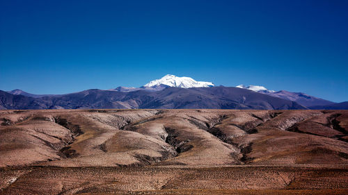 Scenic view of snowcapped mountains and rugged foreground against clear blue sky. 