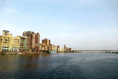City buildings by river against sky