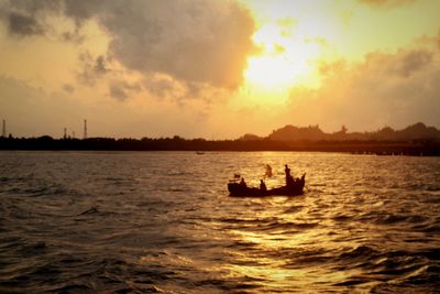 Silhouette people on boat sailing in sea against sky during sunset