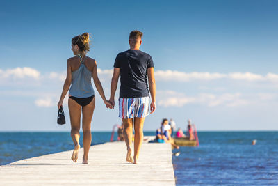 Rear view of people at sea shore against sky