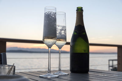 Alcohol bottles on table by sea against sky during sunset