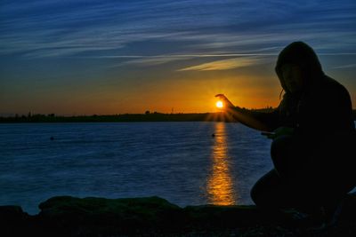 Silhouette woman sitting on beach against sky during sunset