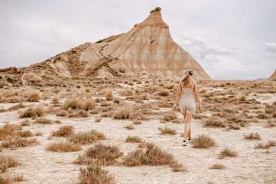 Rear view of woman walking on field against rock mountain