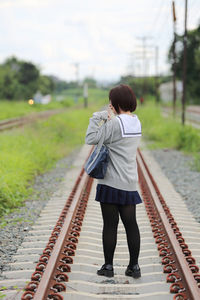 Rear view of young woman in school uniform on railroad track