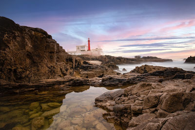 Rocks by sea against sky during sunset