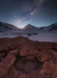 Scenic view of frozen lake by mountain against sky at night