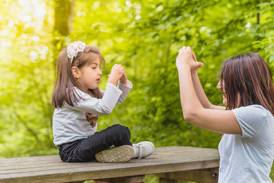 Mother and girl sitting on wood against plants