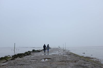 Mid distance view of couple holding hands while standing on pier against sky