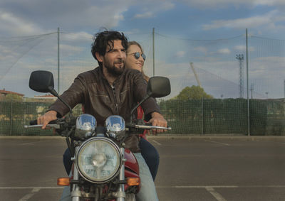 Couple riding motorcycle on road against sky