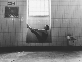 Side view full length of woman sitting with feet up by tiled wall