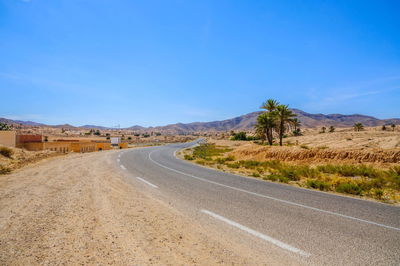 Road leading towards mountains against clear blue sky