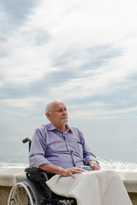 Senior male in wheelchair on promenade looking away in contemplation and enjoying view of sea