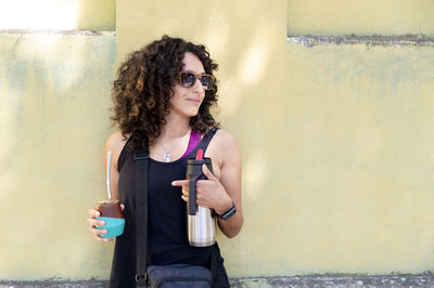 Young woman wearing sunglasses while standing against wall