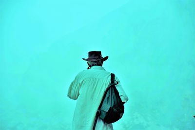 Rear view of man standing against turquoise background