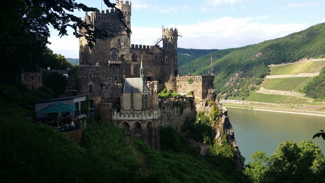 architecture, built structure, building exterior, tree, sky, history, mountain, green color, landscape, the past, cloud - sky, castle, travel destinations, cloud, high angle view, nature, hill, house, tourism, travel