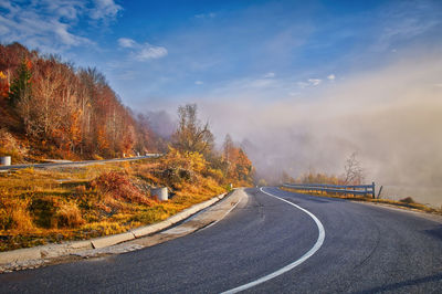 Road by trees against sky during autumn