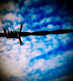 Low angle view of barbed wire against cloudy sky