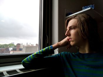 Thoughtful young man looking through window at home