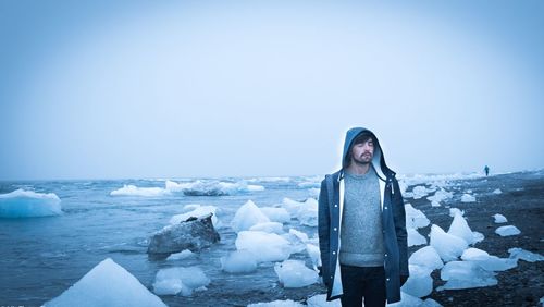 Portrait of young woman standing by frozen lake against clear sky