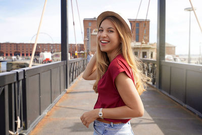 Portrait of smiling traveler girl on swing bridge in royal albert dock, liverpool, uk
