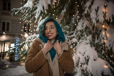Portrait of smiling young woman standing on snow during christmas