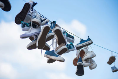 Low angle view of shoes tied on cable against blue sky