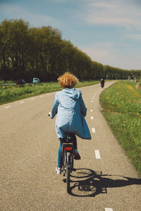 Rear view of woman cycling on road against sky