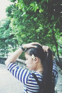 Rear view of young woman tying her hair while standing at public park