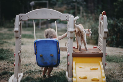Rear view of girl touching kitten while swinging at playground