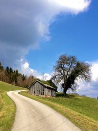 Road amidst field and trees against sky