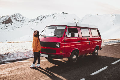 Young happy tourist in eyeglasses standing near vintage automobile between deserted ground in snow near mountains
