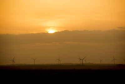 Wind turbines on silhouette landscape against sky during sunset