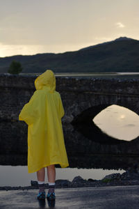 Rear view of woman standing at riverbank against sky