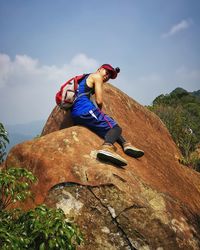 Low angle portrait of young man rock climbing against sky